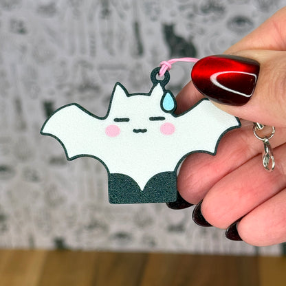 Hand holding a cute white, shy bat-shaped Tab Buddy with a blurred background