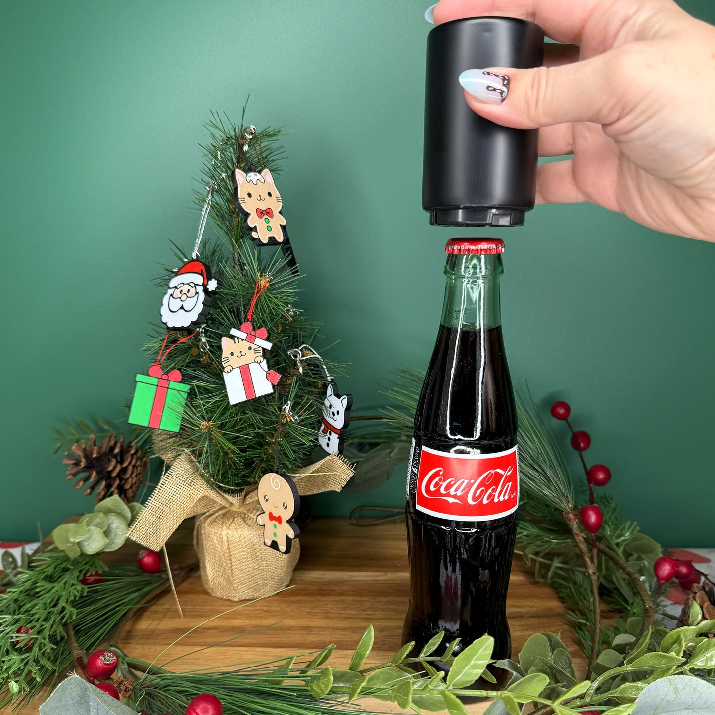Person using a bottle opener on a Coca-Cola bottle with a Christmas tree and decorations in the background.