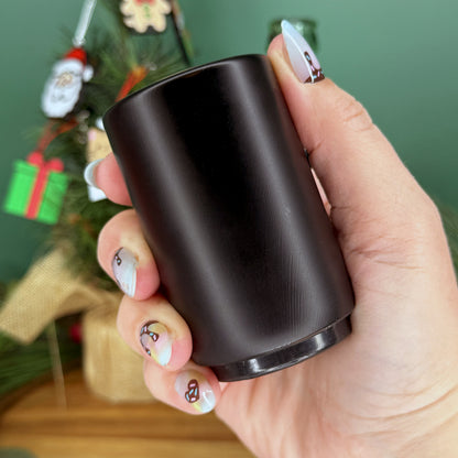 Hand holding a black bottle opener with a Christmas tree in the background