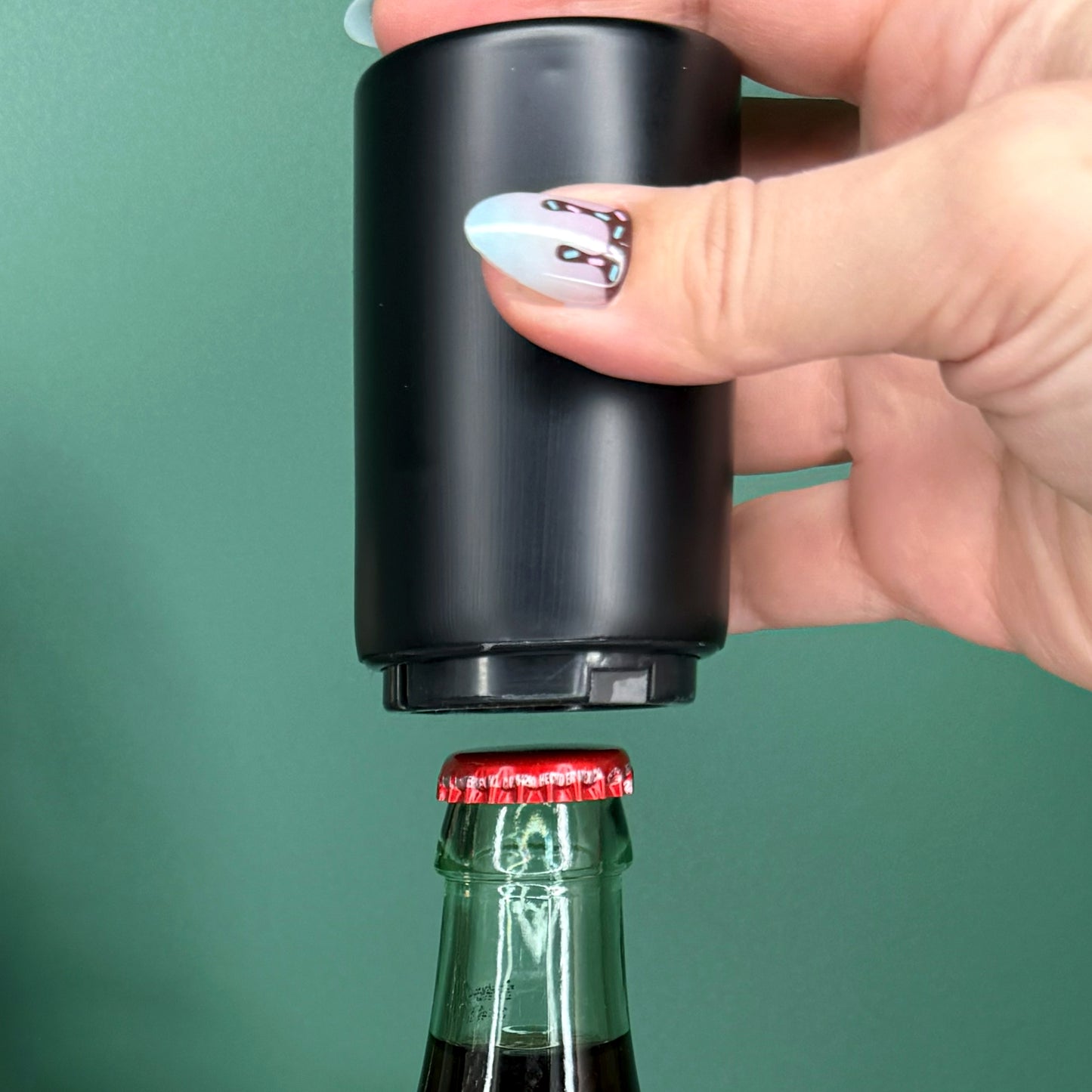 Hand using a black bottle opener on a green background