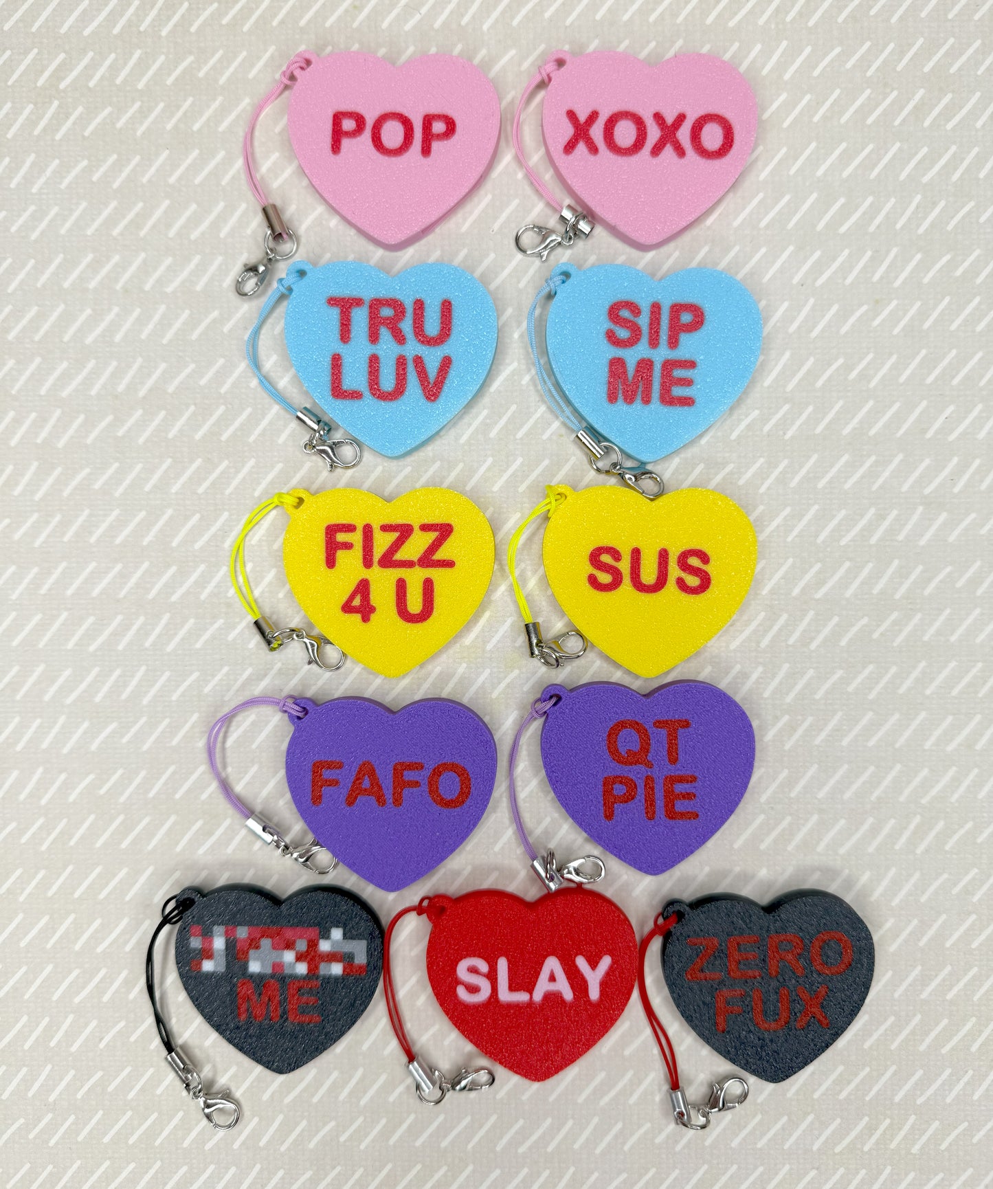 Heart-shaped Tab Buddy keychains with various phrases on a textured white background