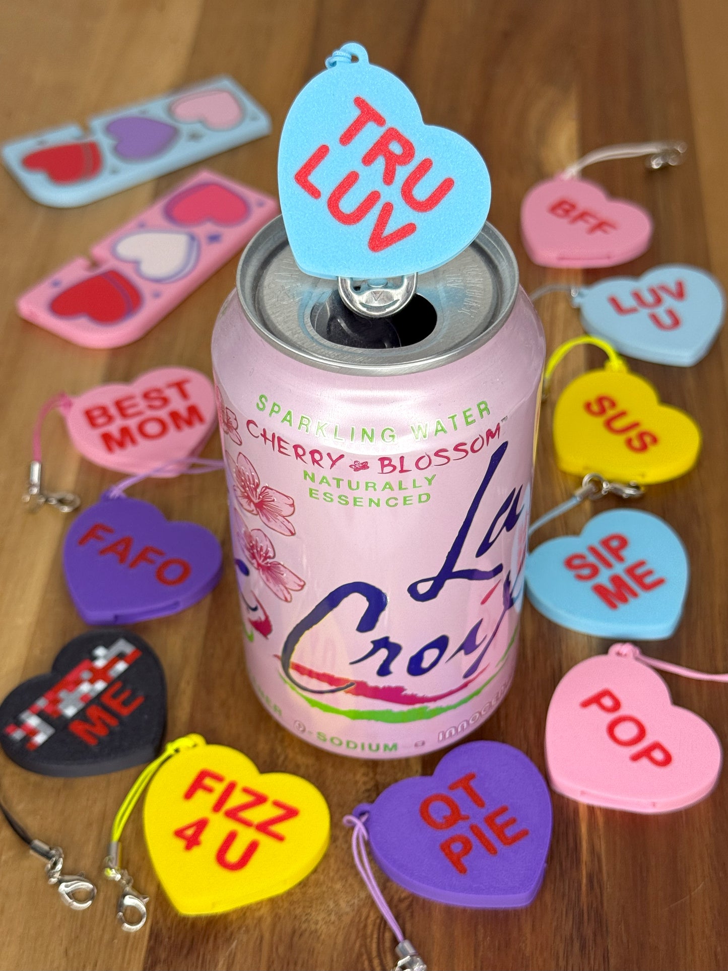 Pink La Croix can surrounded by colorful heart-shaped Tab Buddes on a wooden surface