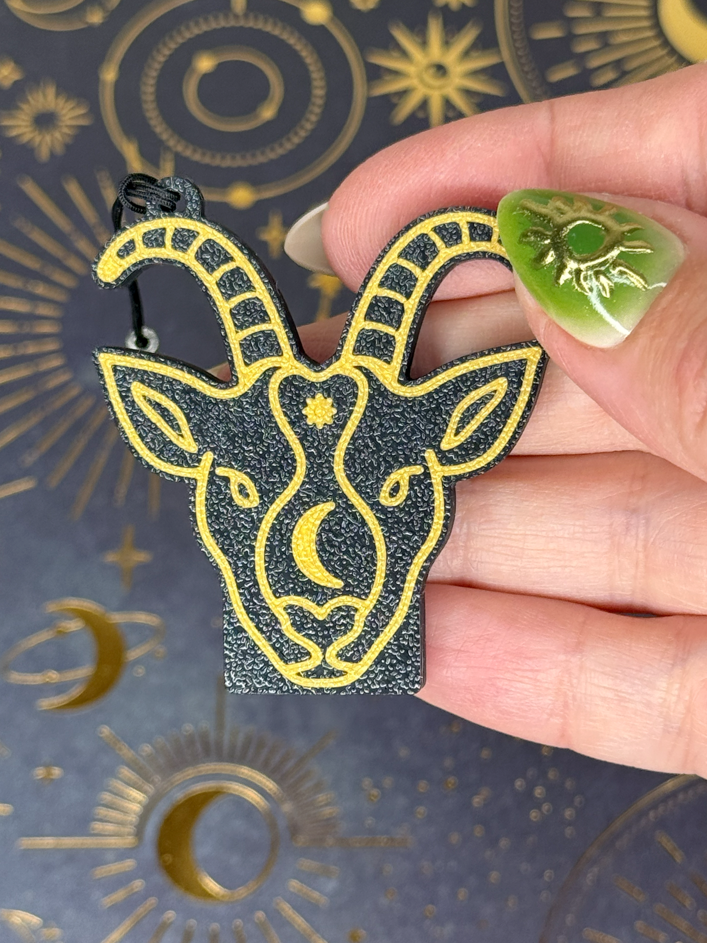 Hand holding a black and gold Capricorn goat head Tab Buddy against a dark background with celestial designs.