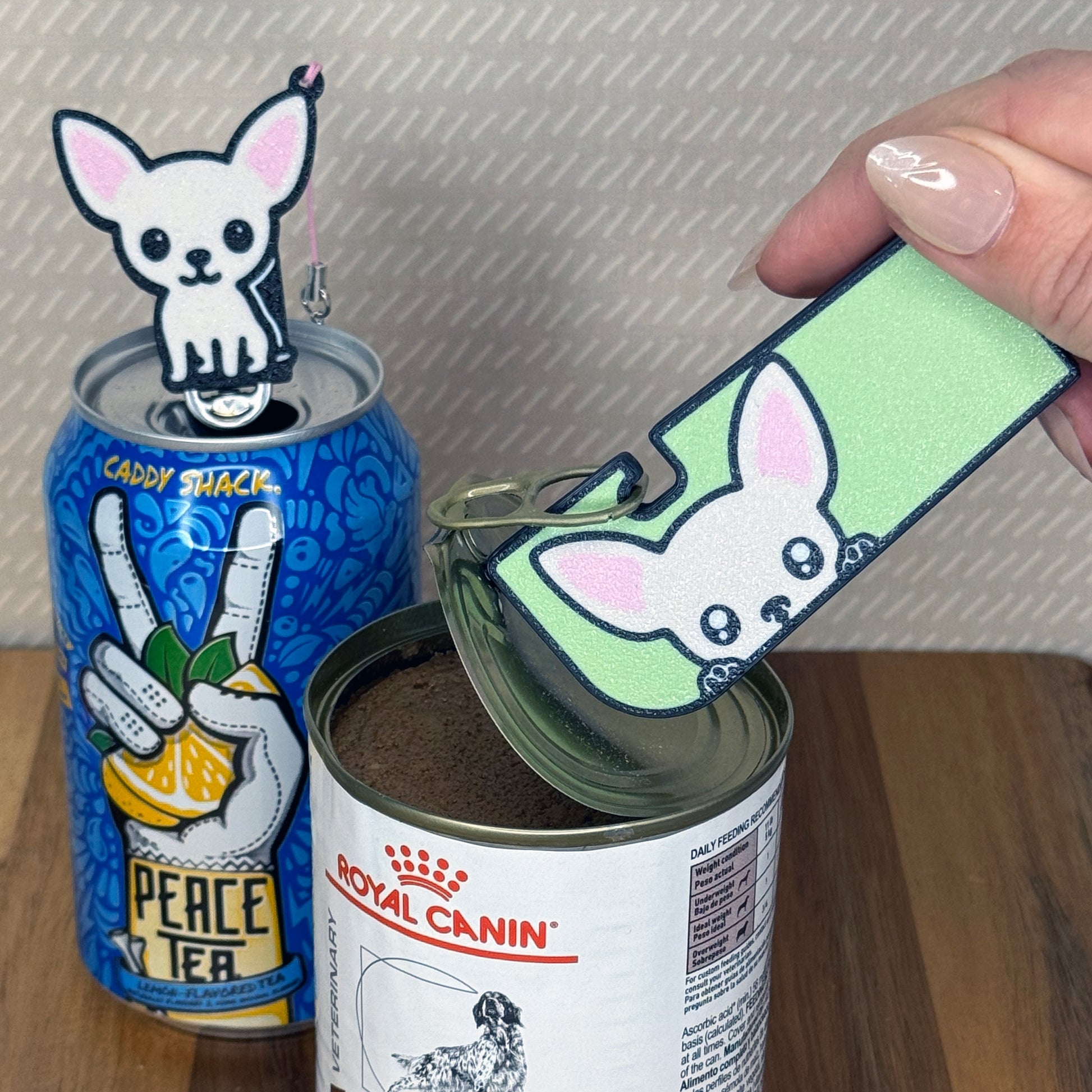 A matching set of Chihuahua-inspired Tab Buddies are shown. The soda-sized Tab Buddy rests atop a blue soda can, and the Tab Buddy XL is used to peel back a can of dog food.