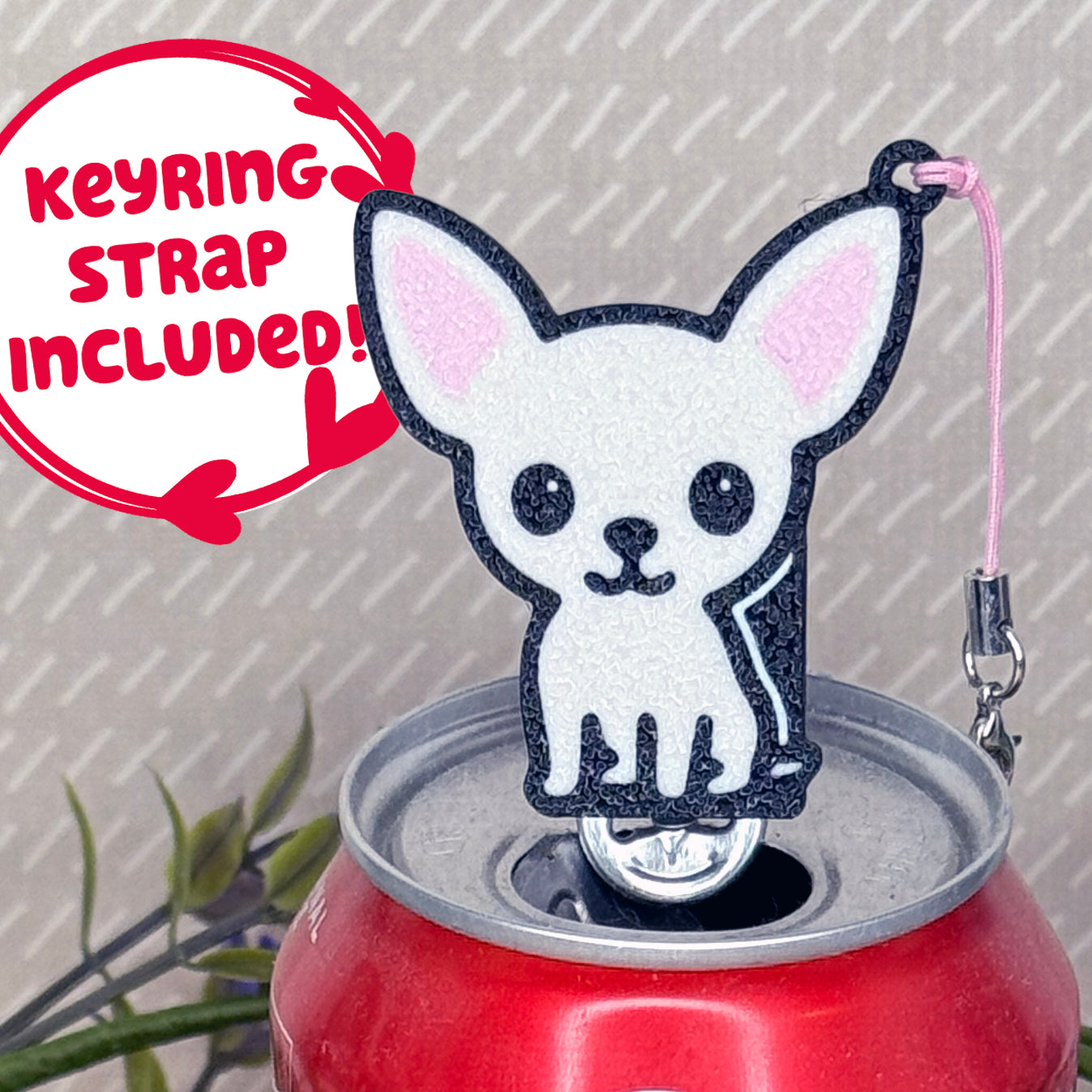 A cream Chihuahua-inspired Tab Buddy rests atop an open can tab. Desecriptive text reads "Keyring Strap Included!"