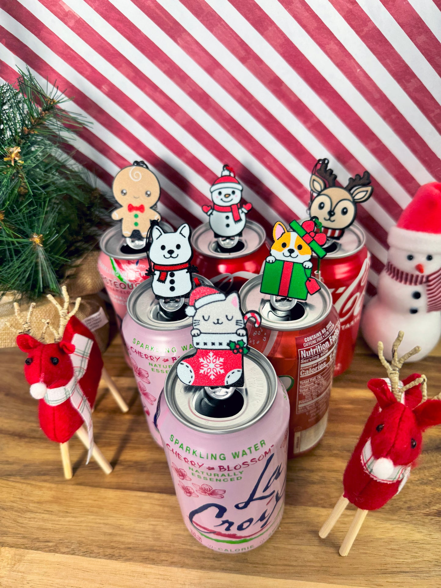 Festive Christmas Tab Buddies rest atop soda cans with a striped background