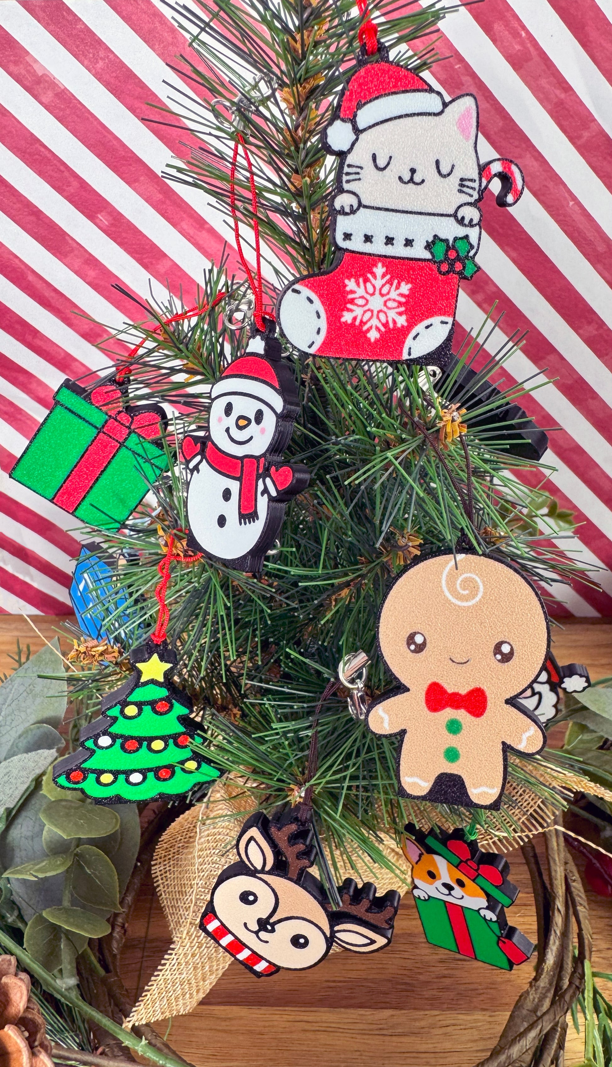 Festive Christmas-themed Tab Buddies hang by their straps from a Christmas tree with a striped red and white background