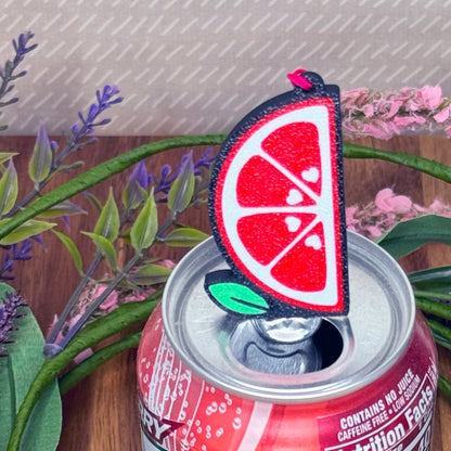 Red soda can with a Tab Buddy featuring a grapefruit slice design, surrounded by plants.