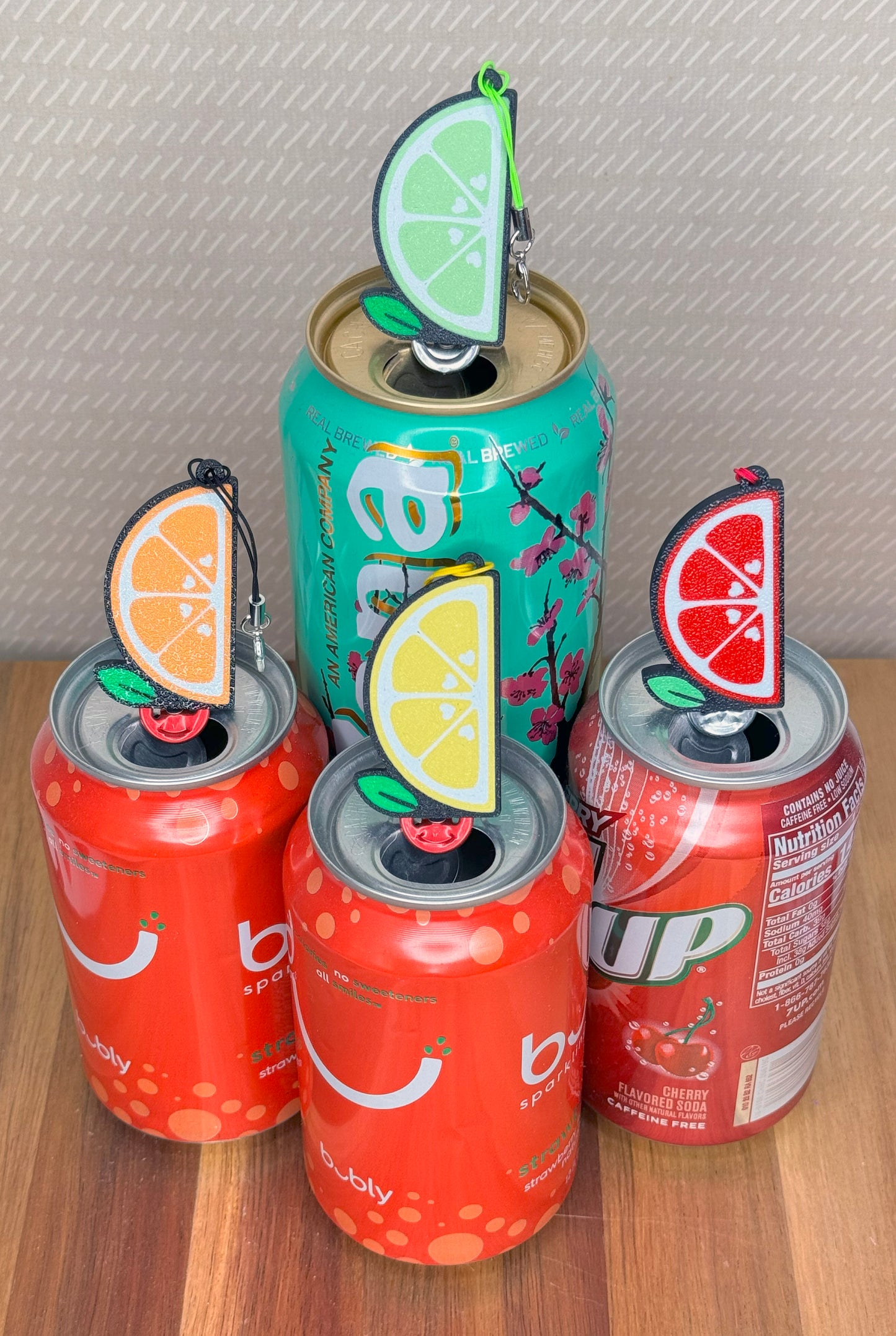 Four soda cans with decorative fruit slice Tab Buddies of various colors on a wooden surface