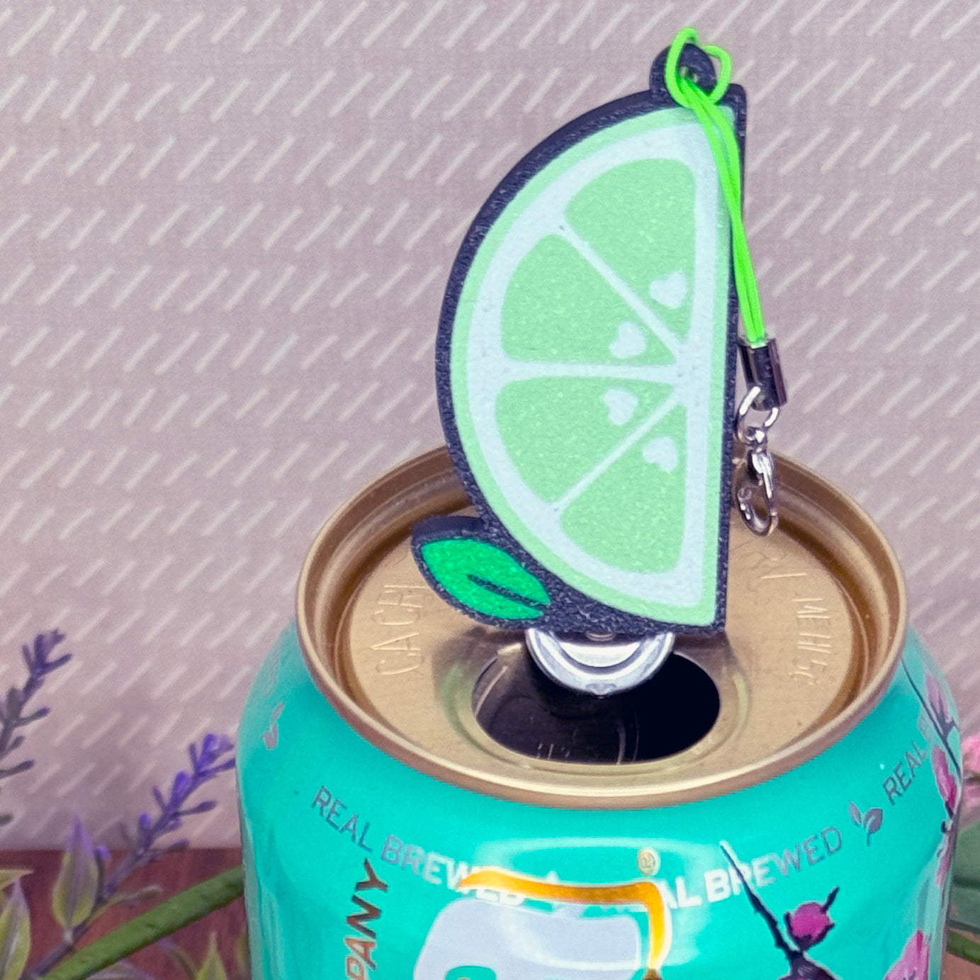 Lime slice Tab Buddy keychain sits atop a can with a patterned background