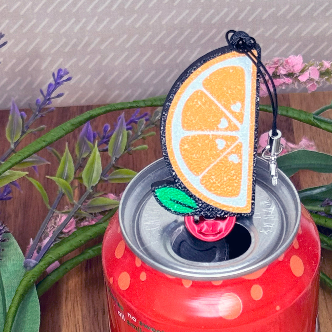Orange slice Tab Buddy keychain on a red can with plants in the background