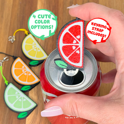 A Tab Buddy with a red grapefruit slice design sits atop a can, surrounded by lemon, orange, and lime design Tab Buddies.