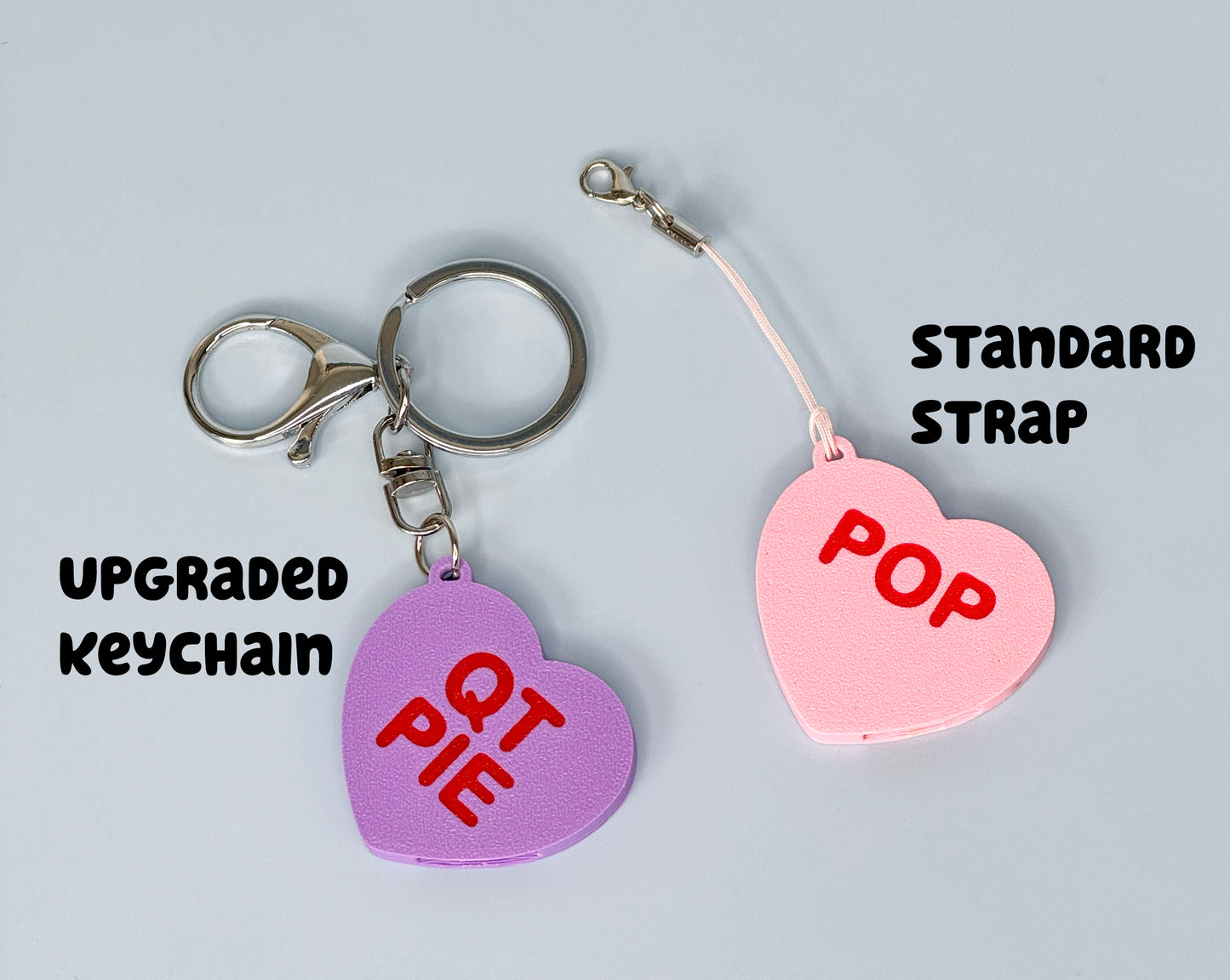 Two heart-shaped Tab Buddies are shown - one with a standard strap and one with upgraded keychain.