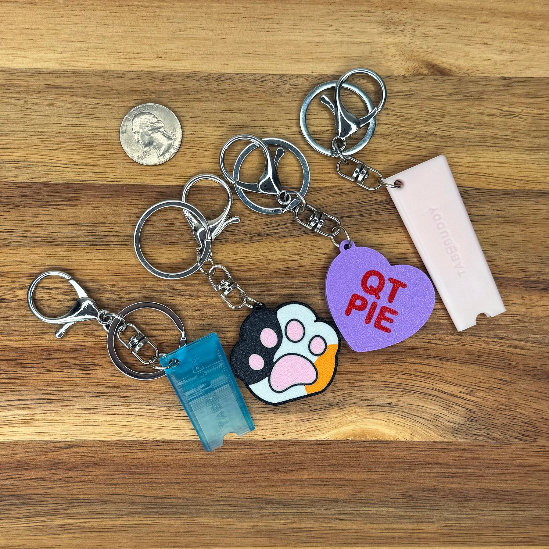 Various Tab Buddies are shown with optional keychains attached on a wooden surface.