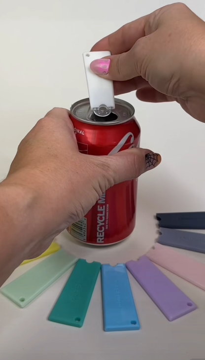 Person using a white Tab Buddy Classic to open a red Coca-Cola can with other colorful Tab Buddy Classics arranged in a circle around the can.