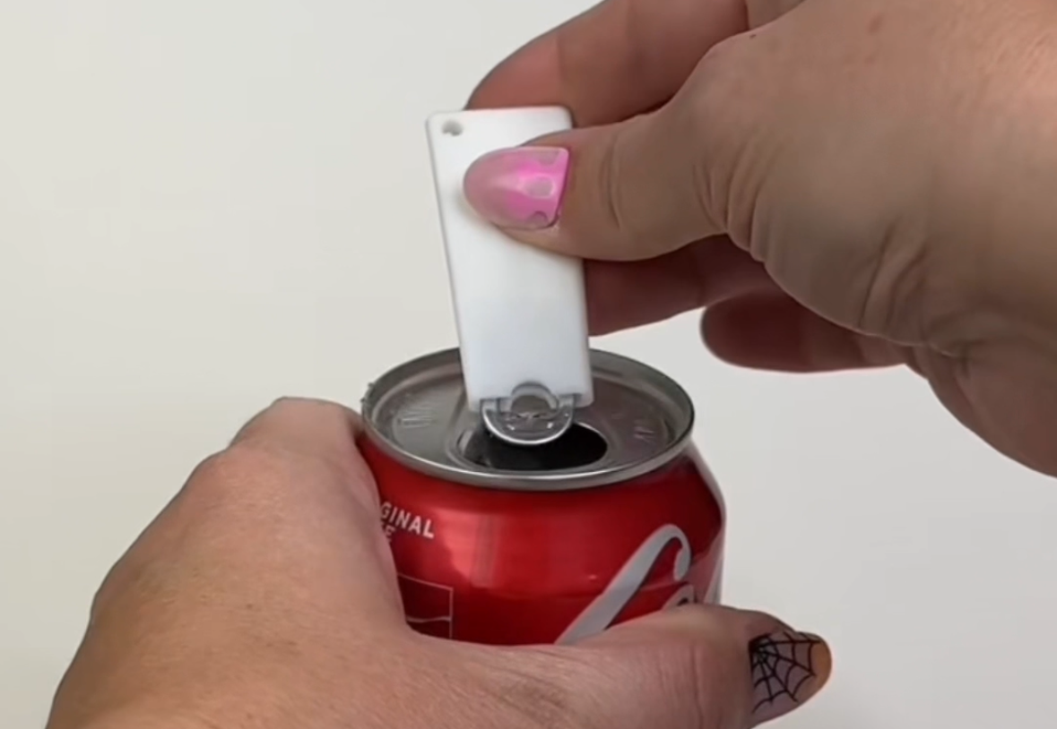 A white Tab Buddy Classic is used to open a red can of soda.