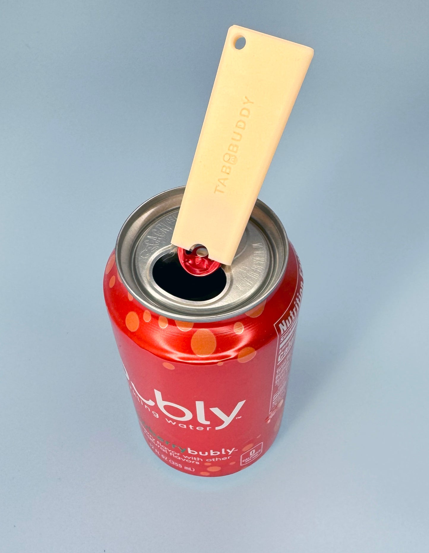 A peach-colored Tab Buddy Classic sits atop a red can of Bubly sparkling water