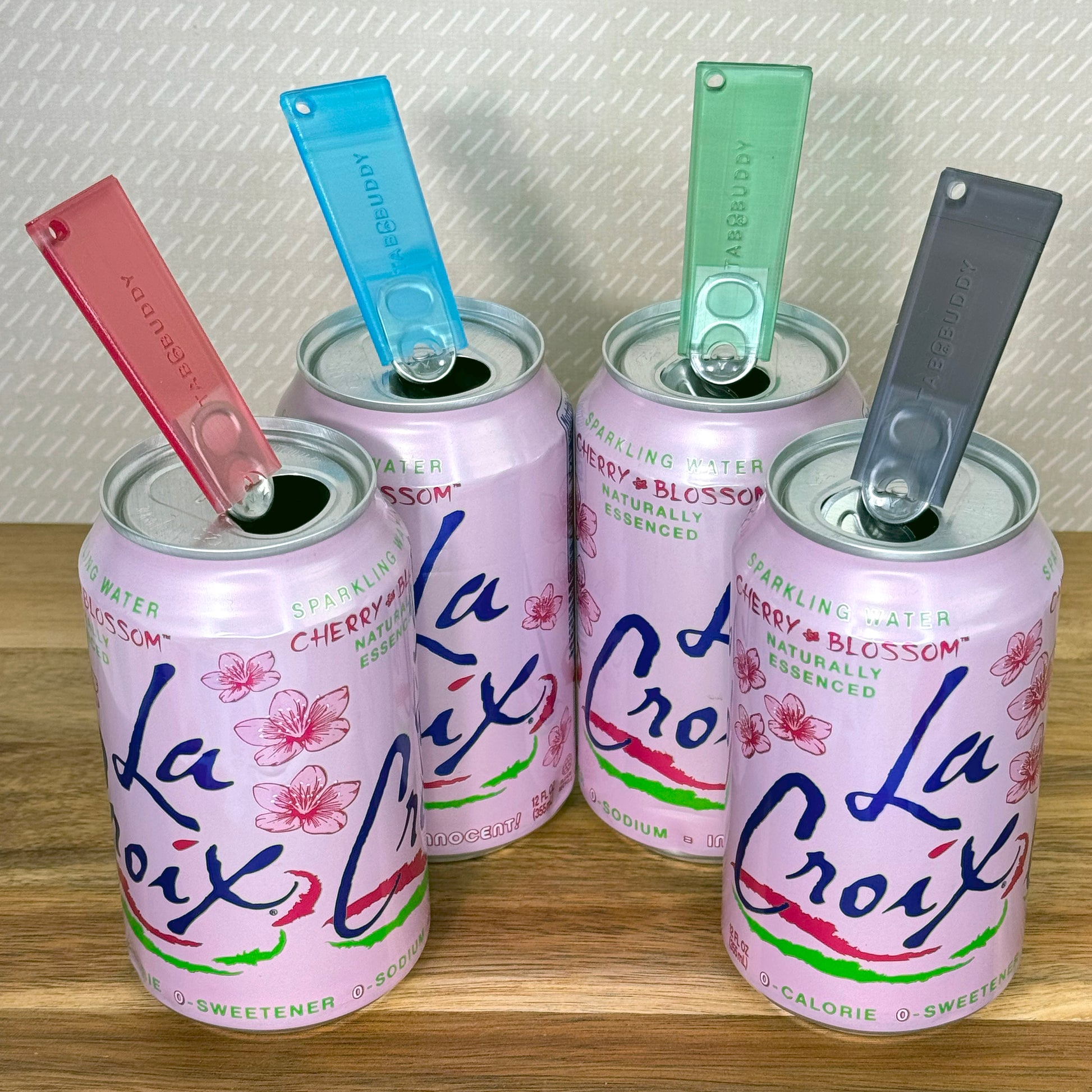 Four pink La Croix cans with colorful Tab Buddy Classics on a wooden surface.