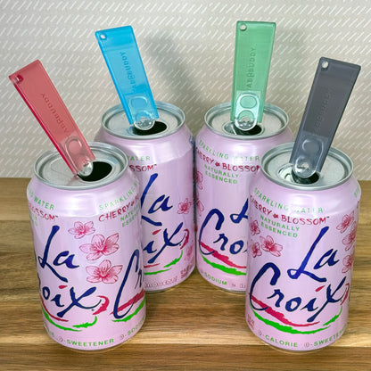 Four pink La Croix cans with colorful Tab Buddy Classics on a wooden surface.