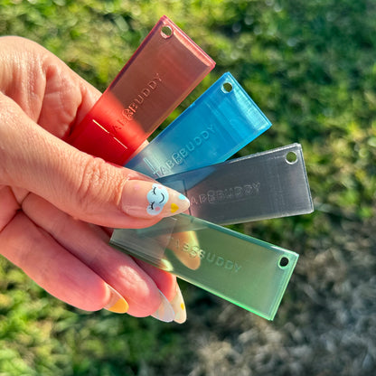 Hand holding four colorful, transluscent Tab Buddy Classics against a grassy background