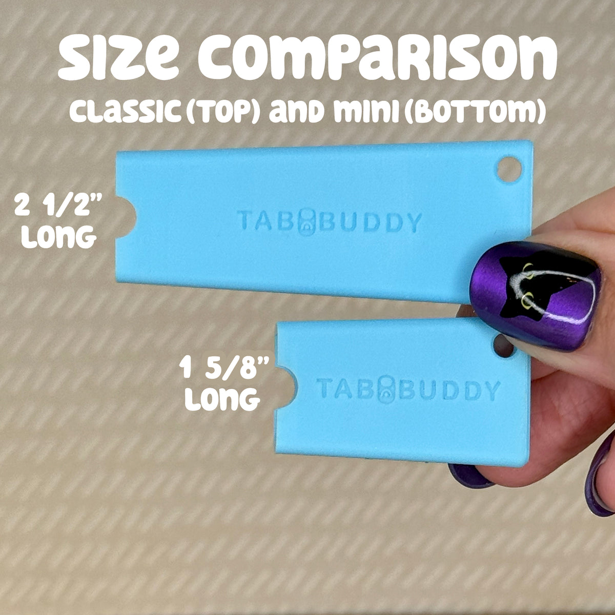 A hand with purple nail polish holds a Sky Blue Tab Buddy Classic and Tab Buddy Mini, comparing their sizes. The Classic is labeled as 2 1/2" long, and the Mini as 1 5/8" long.