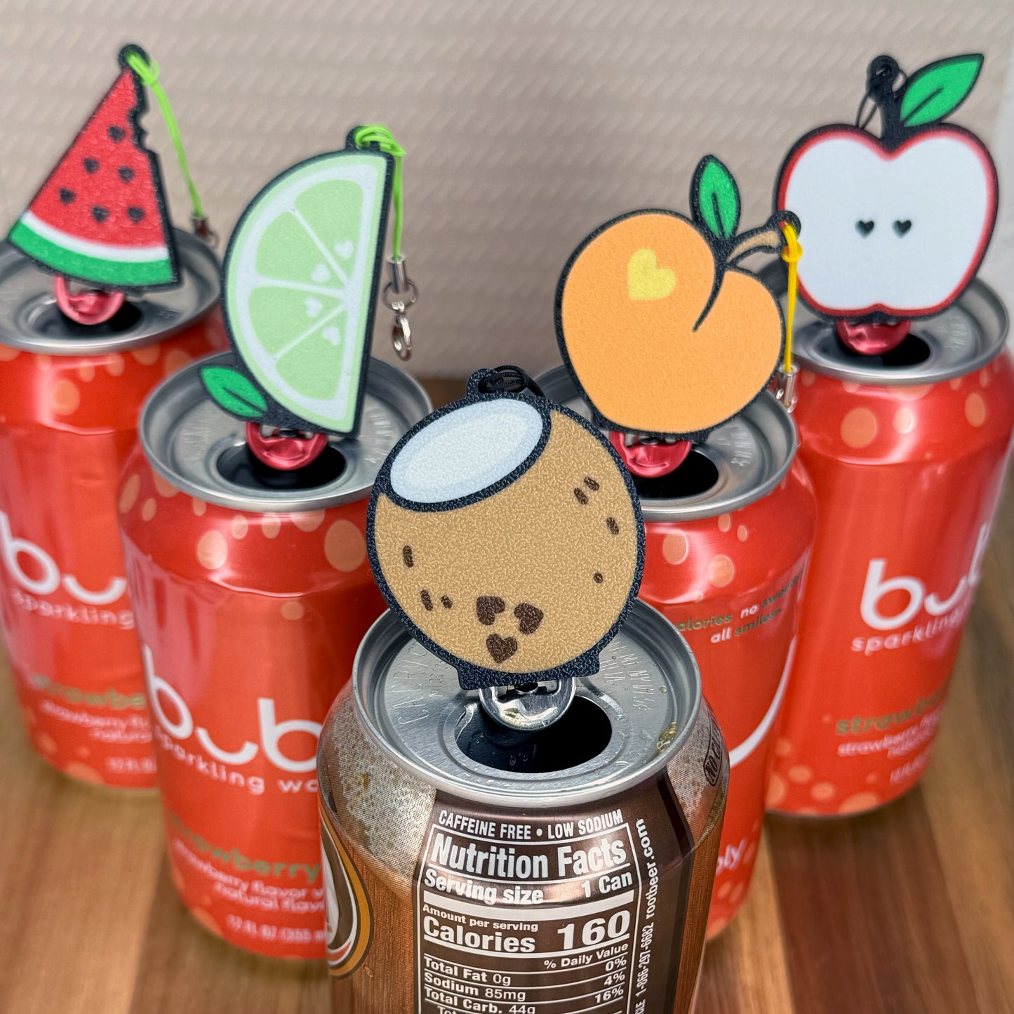 Red cans with fruit-themed Tab Buddies on a wooden surface