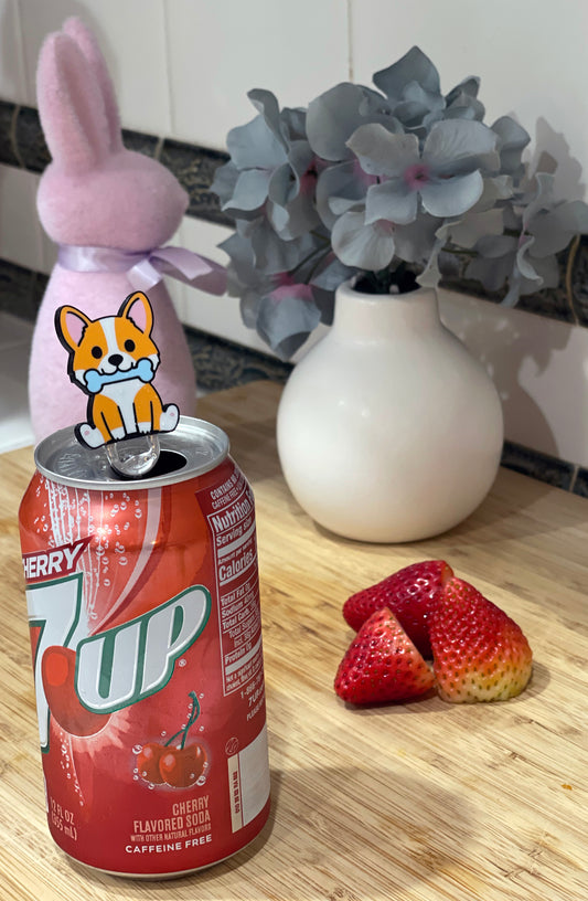 Soda can with a dog Tab Buddy on top, next to strawberries and a decorative vase with flowers.