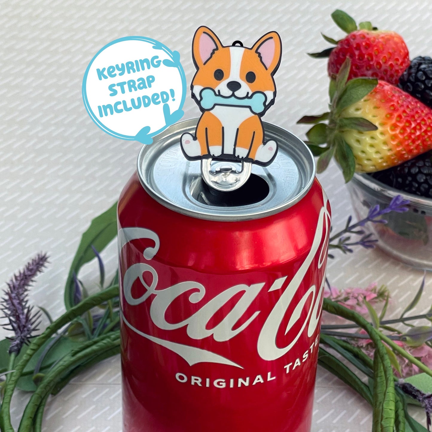 Can with a dog-shaped Tab Buddy on top, surrounded by strawberries and flowers, text says 'keyring strap included!'