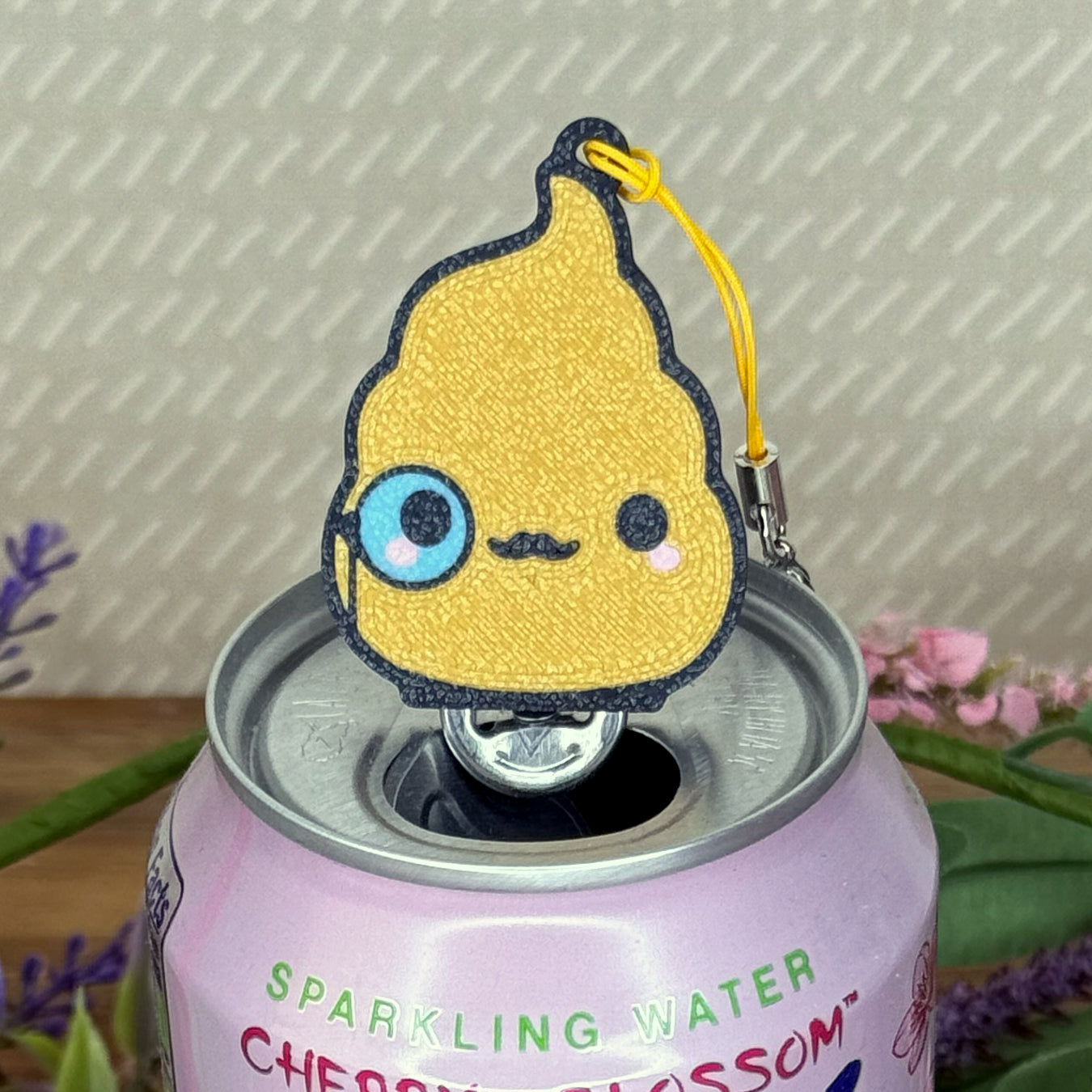 Golden poop emoji-shaped Tab Buddy with mustahe and monacle sits atop a can of sparkling water with a floral background. 