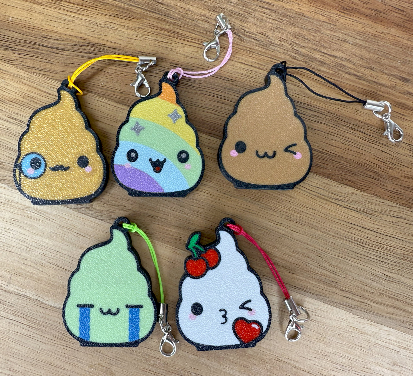 Five colorful poo-shaped Tab Buddy keychains in different color options are shown on a wooden surface