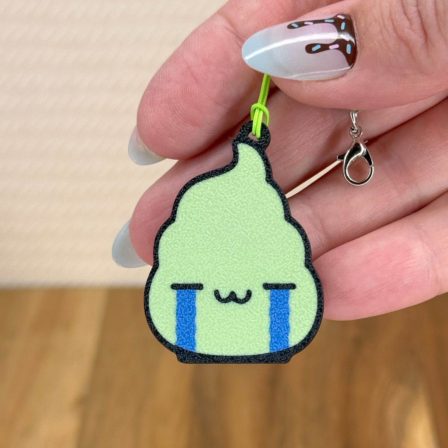 Hand holding a design of a dollop wasabi with a crying face Tab Buddy on a wooden surface.