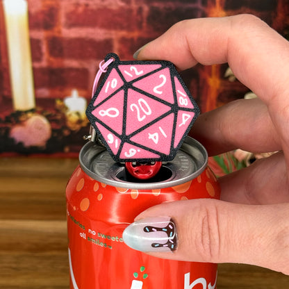 Pink D20 dice Tab Buddy held by a hand on a wooden surface