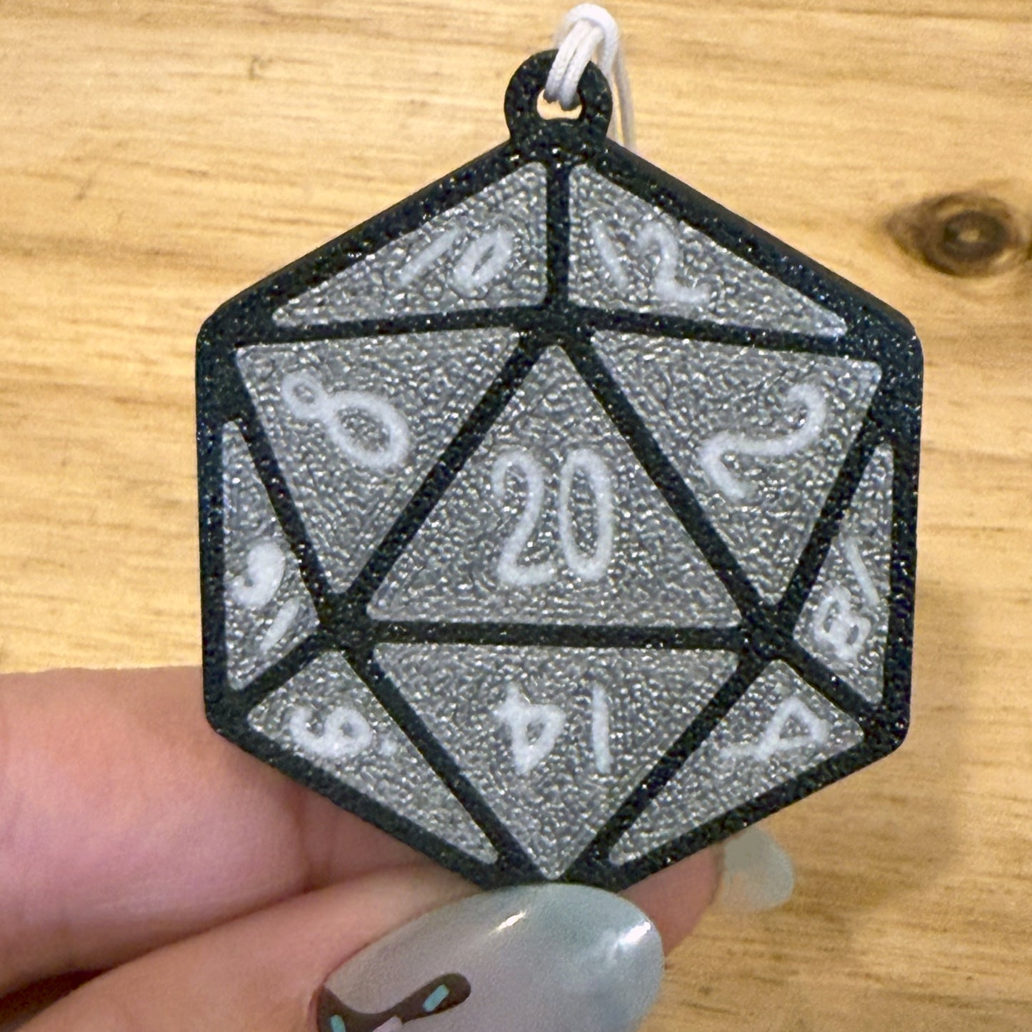 Silver D20 dice Tab Buddy held by a hand on a wooden surface