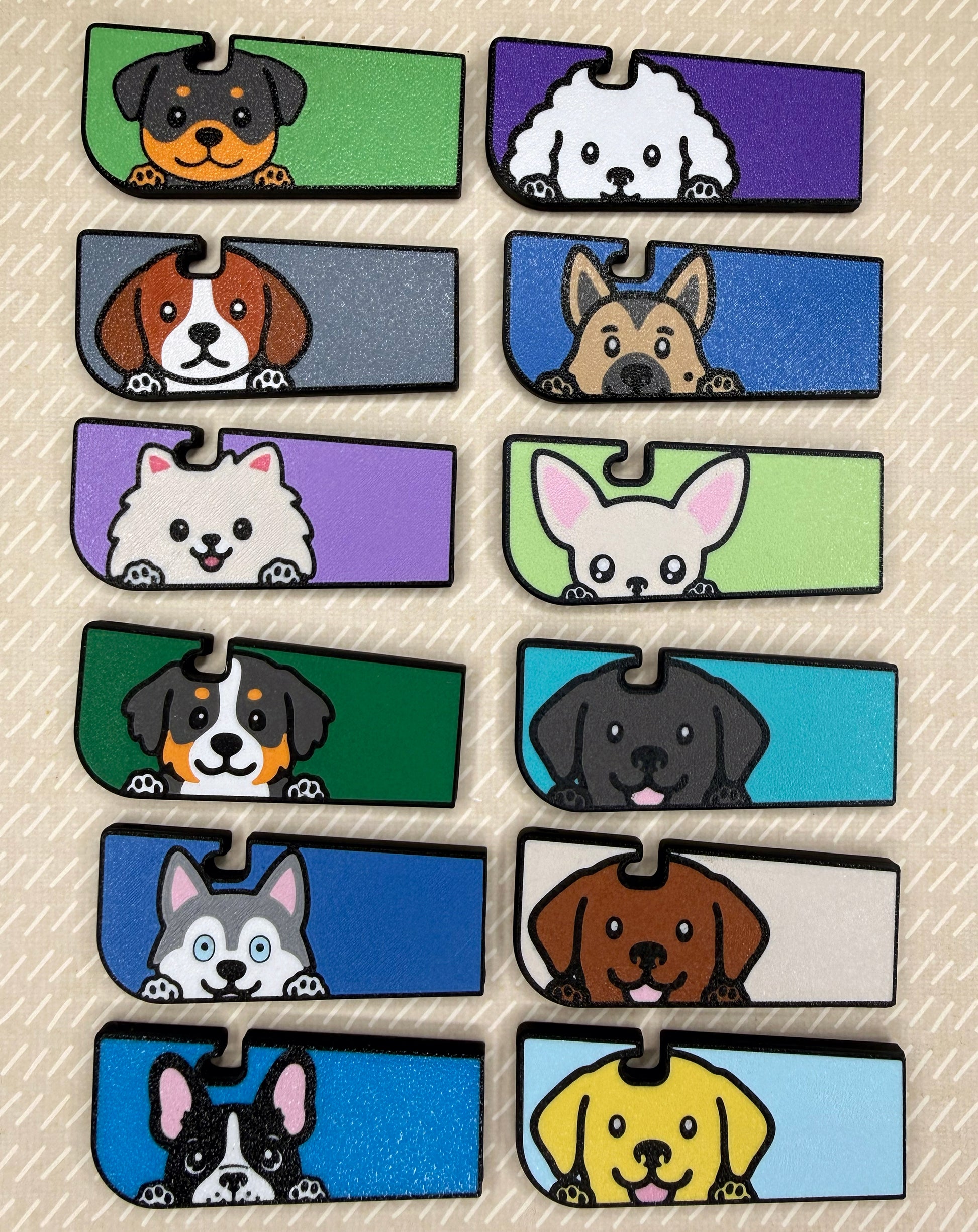 A collection of 12 dog-themed Tab Buddy XLs with colorful backgrounds and cartoon-style dogs are shown resting atop a beige background.