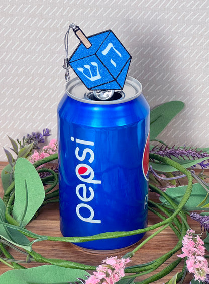 Soda can with a blue dreidel Tab Buddy on top, surrounded by greenery and flowers