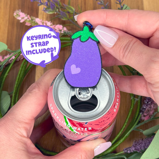 Tab Buddy shaped like an eggplant with a keyring strap sits atop a can with flowers in the background