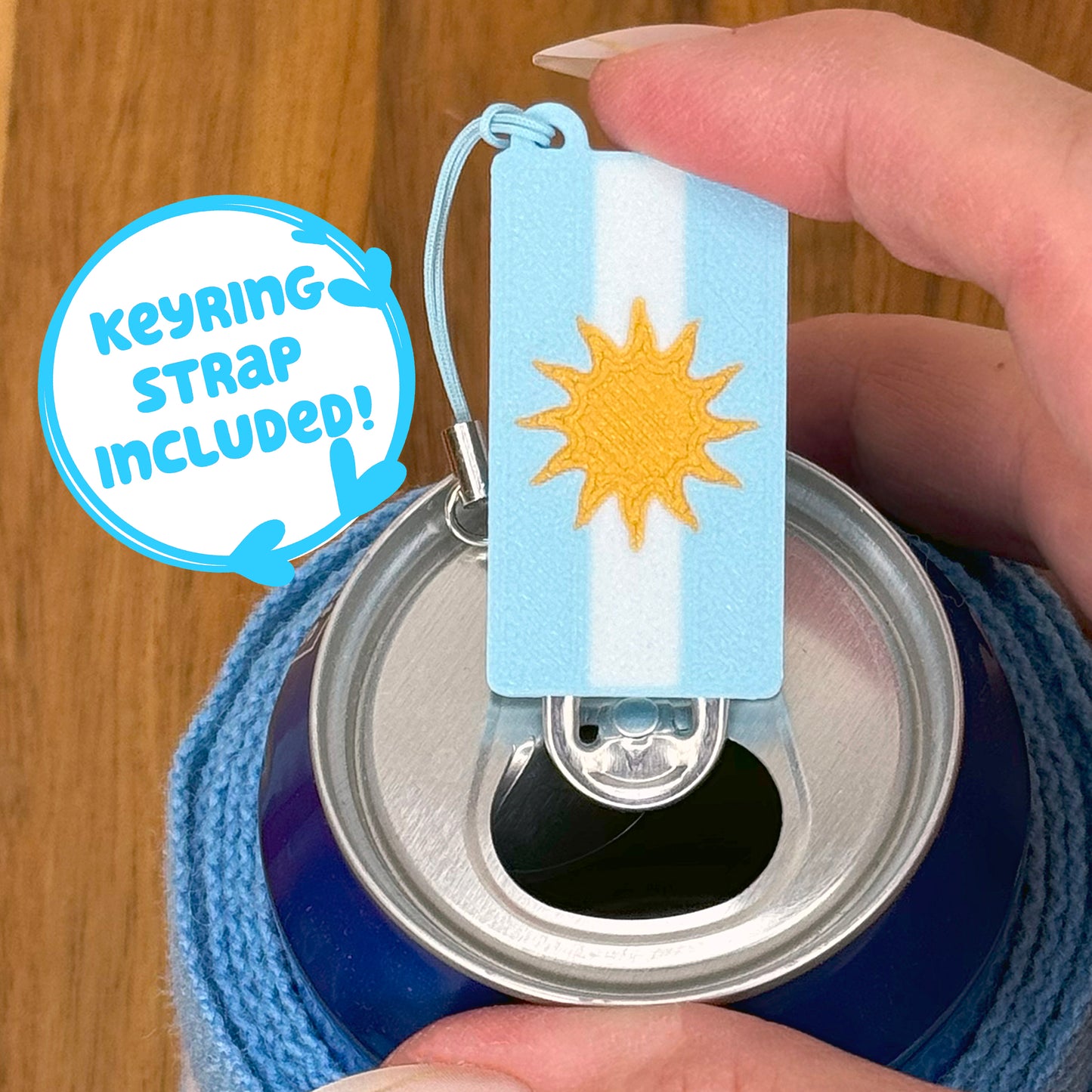 Tab Buddy with Argentina flag design sits atop a soda can, held by a hand.