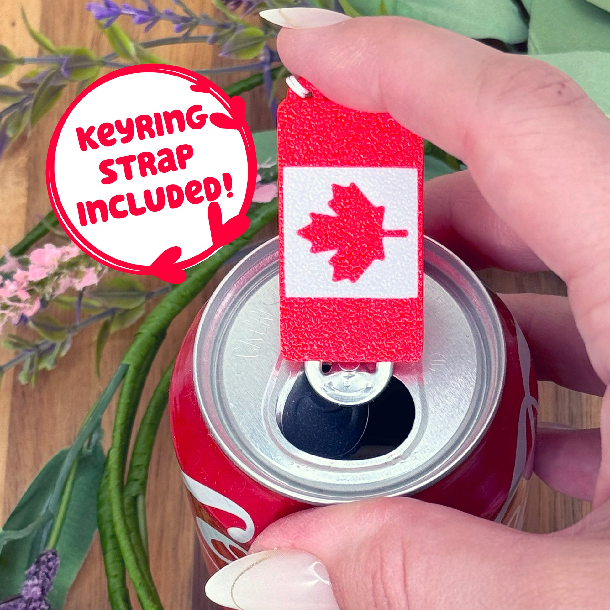 Hand holding a can with a Canadian flag Tab Buddy, surrounded by plants.