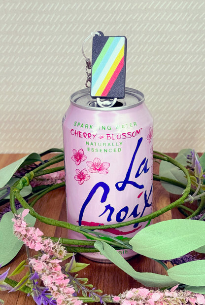 Pink La Croix can with disability flag Tab Buddy on a wooden surface with greenery and flowers.