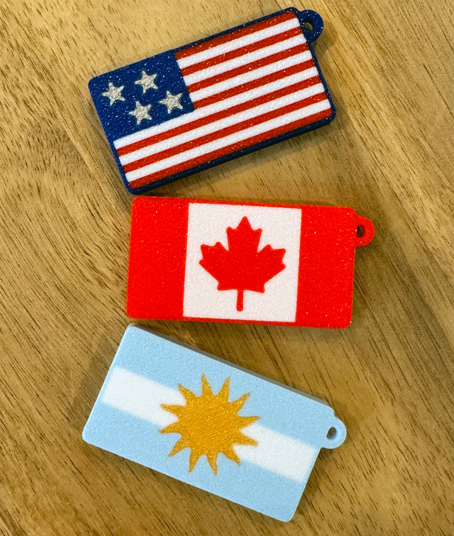 Three flag-themed Tab Buddies keychains on a wooden surface