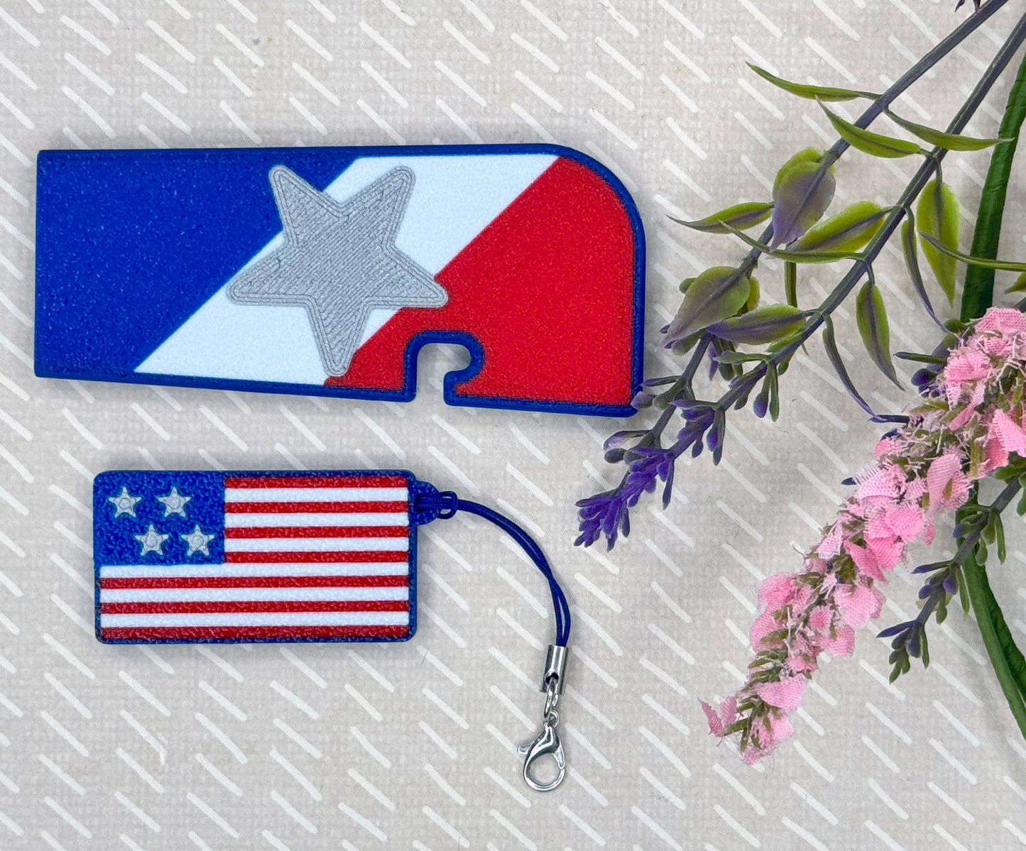 Two USA patriotic flag-themed Tab Buddies -- one soda sized and one XL -- on a textured surface with flowers