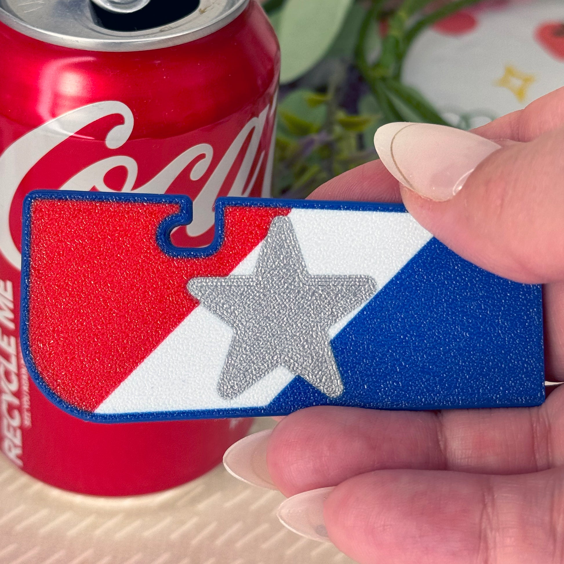 Hand holding a patriotic red, white and blue Tab Buddy XL with a Coca-Cola can in the background