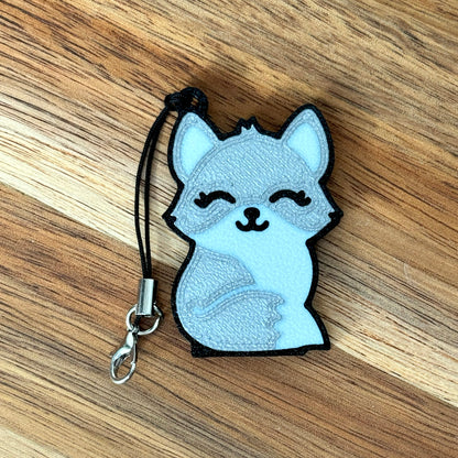 Tab Buddy Keychain with a cartoonish silver fox design on a wooden surface