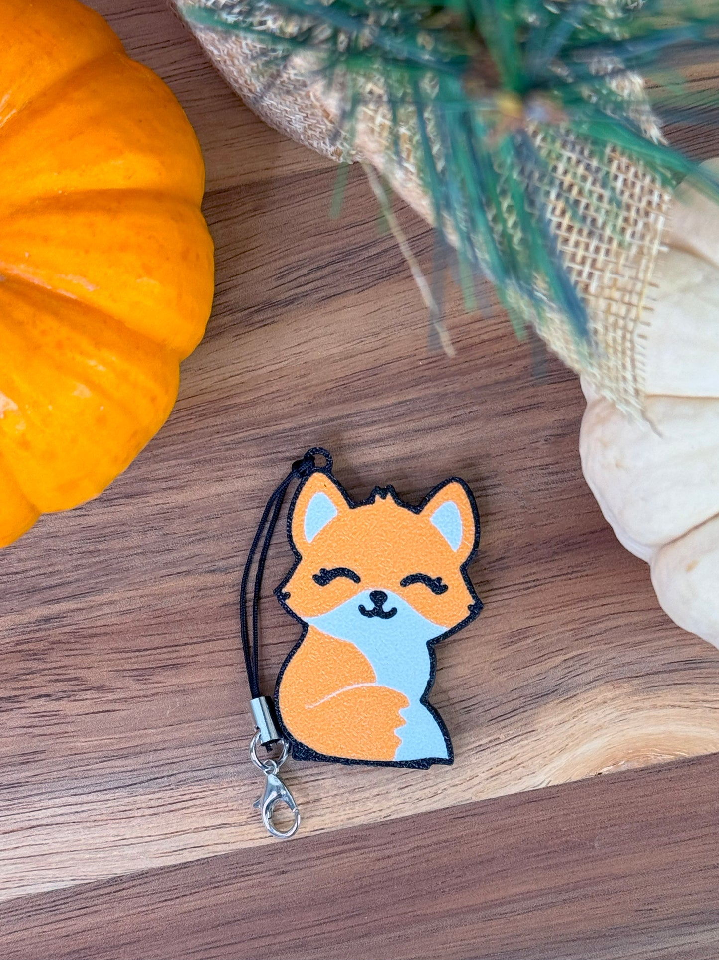 Fox-shaped Tab Buddy on a wooden surface with pumpkins and a plant in the background
