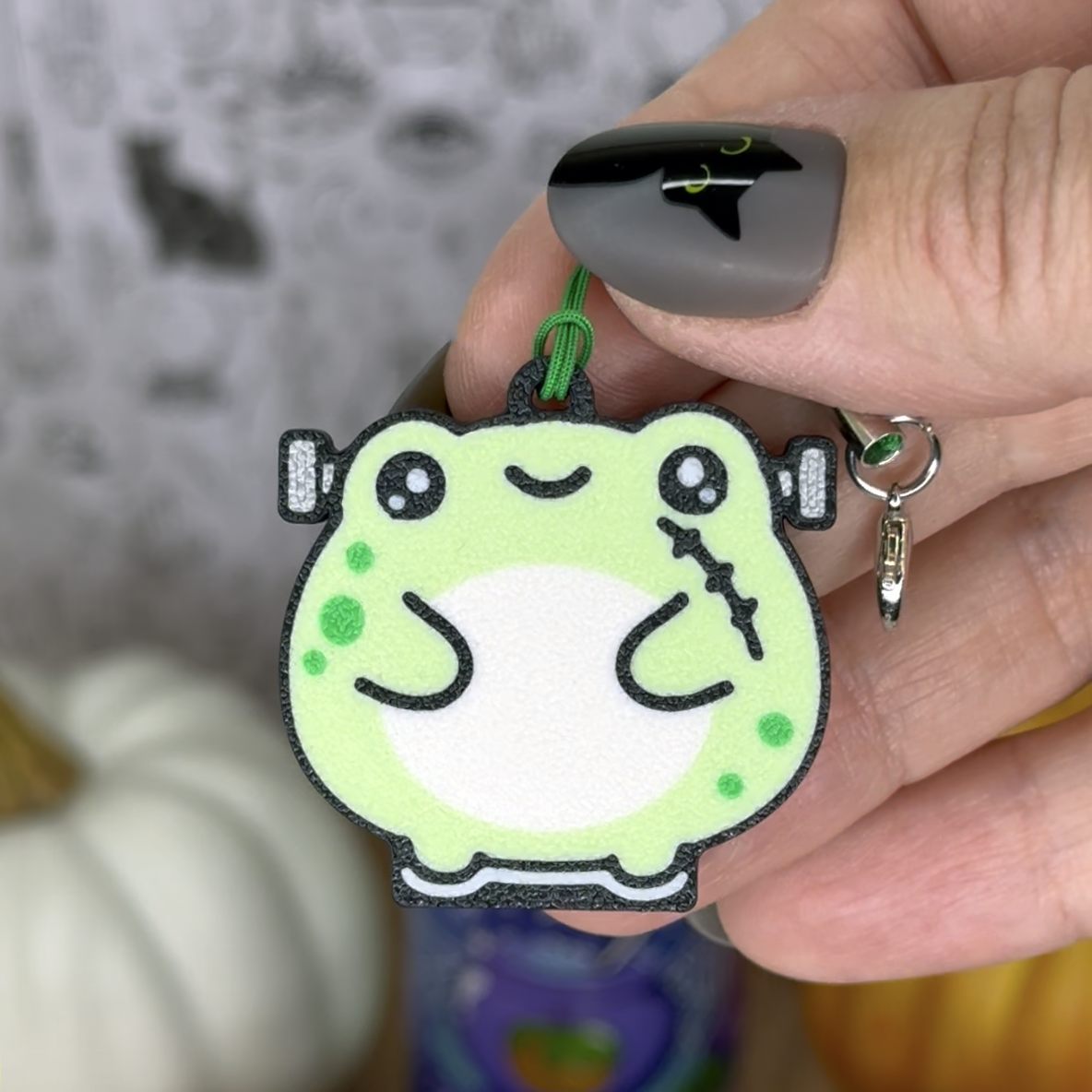 Hand holding a green Frankenstein's Monster frog  Tab Buddy keychain with a blurred background