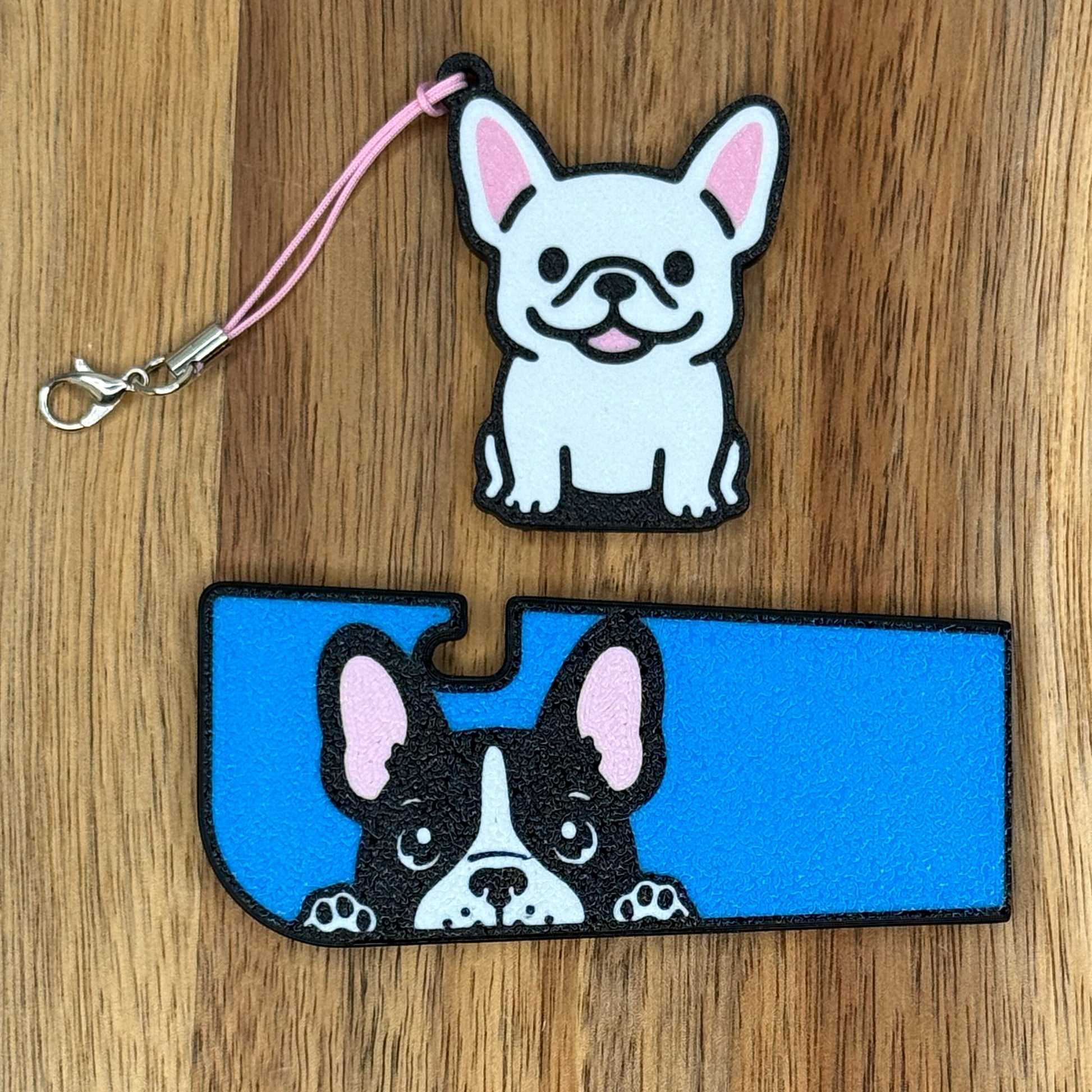 A set of French Bulldog-inspired soda Tab Buddy and Tab Buddy XL rest atop a wooden surface.