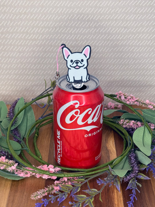 A White French Bulldog-inspired Tab Buddy rests atop an open can tab with a beige background and floral accents.