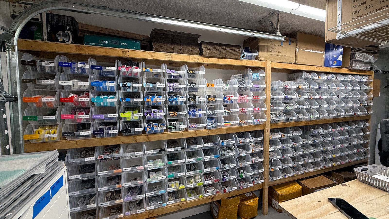 Shelving unit with labeled clear containers full of Tab Buddies in a small workshop setting