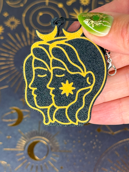Gemini Zodiac Tab Buddy Keychain with astrological design held by a hand against a celestial pattern background