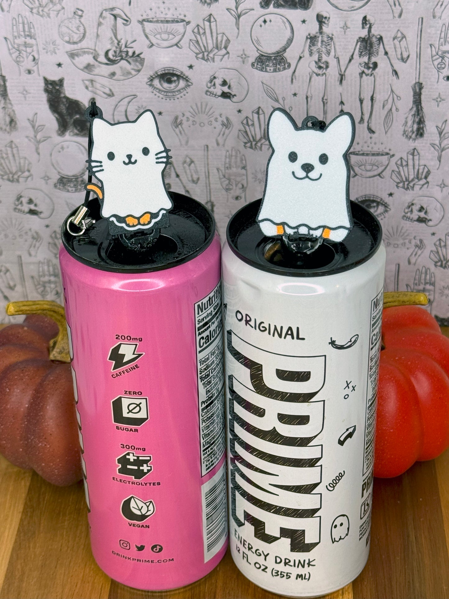 Two energy drink cans with ghost caat and ghost dog Tab Buddies on a wooden surface.